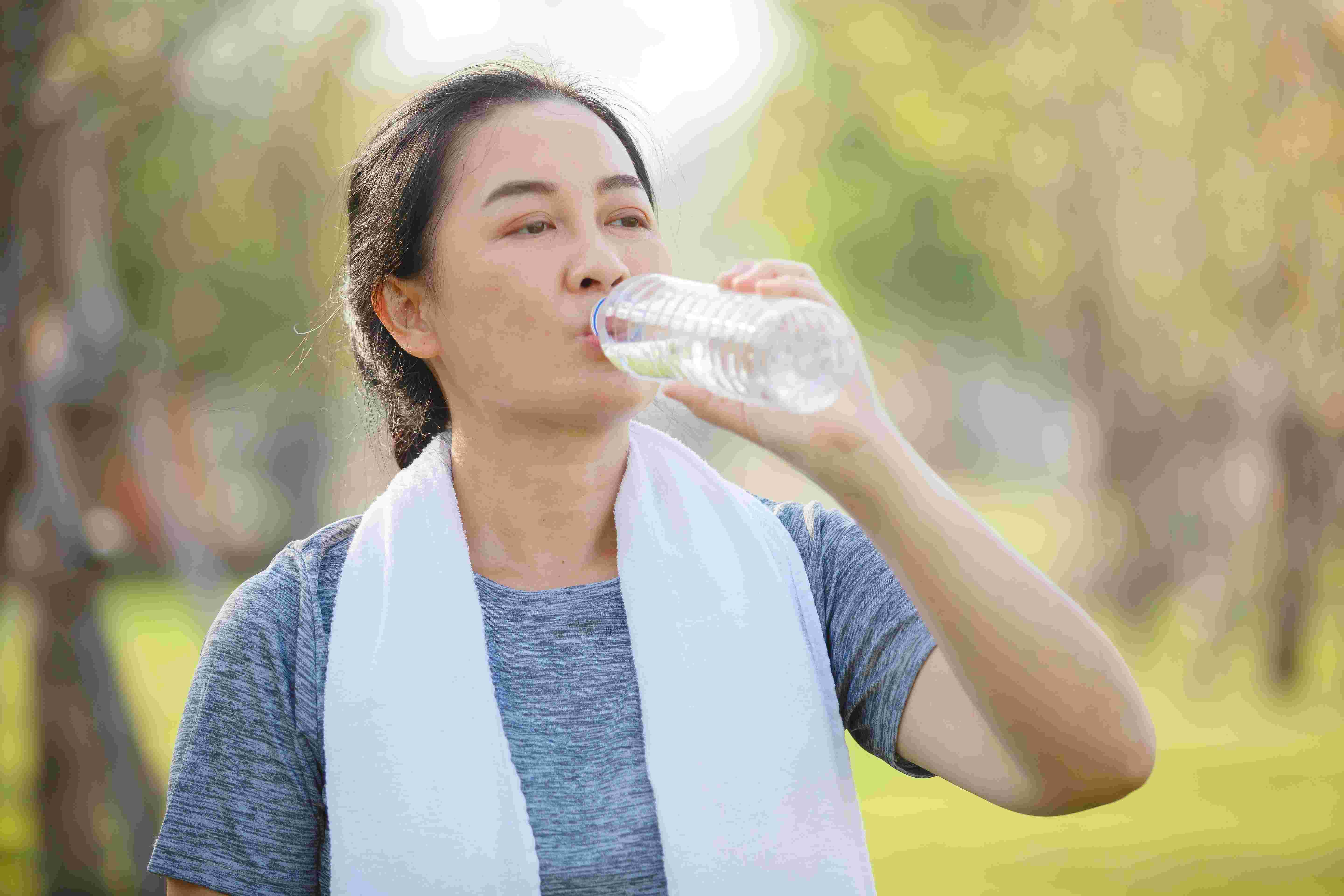 Woman with towel on neck drinking water after exercising while on dialysis