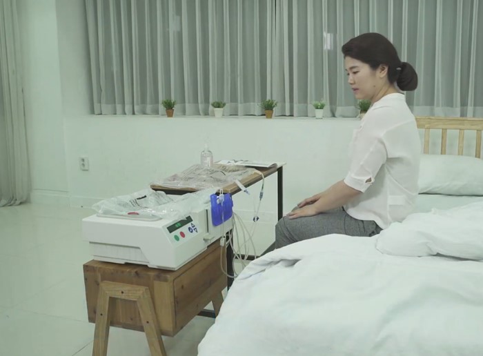Woman sitting on bed in room preparing for peritoneal dialysis