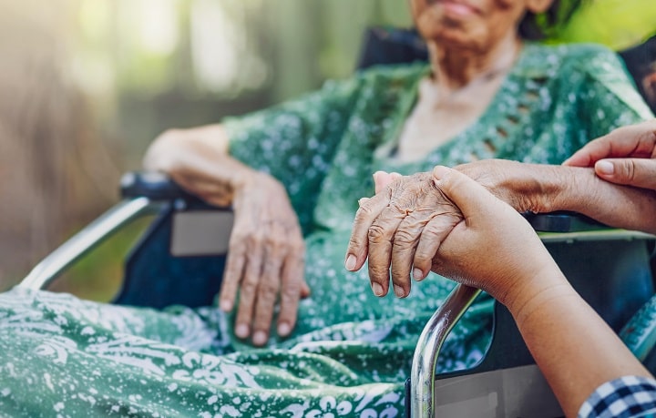 Holding hand of elderly woman sitting on wheelchair